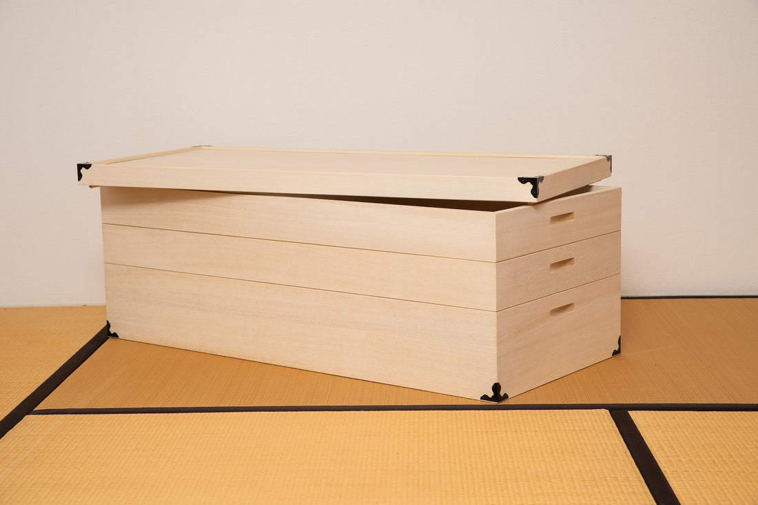 A paulownia wood kimono box with a hinged lid, partially open to reveal its spacious interior. The box is designed with clean lines and traditional hardware, placed on a tatami floor, highlighting its minimalist and elegant design.