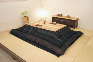 A high-quality Japanese kotatsu table with a thick, patterned dark futon quilt in a minimalist interior.