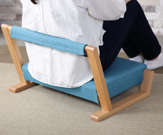 A person sitting on a ZAGAKU Japanese floor chair with blue upholstery, providing ergonomic back support for floor sitting.